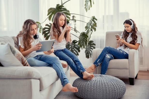 Education, friendship, technology and children concept. Group of teenage girls is using gadgets. Kids with phones and tablets, with smartphones and headphones.
