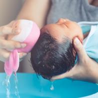 Cute asian newborn baby girl take a bath. Mom cleaning her baby hair with sponge.