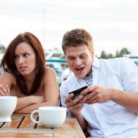 Photo a young couple having a disasterous first date.  Young woman looks annoyed as her date seems more excited about his phone than he is about being with her.