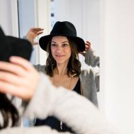 Mature woman standing in front of mirror , putting on a hat