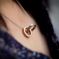 A necklace with two joined rings, representing friendship or love. Very romantic, shallow focus with other elements blurred out creatively.  Gold and Silver.