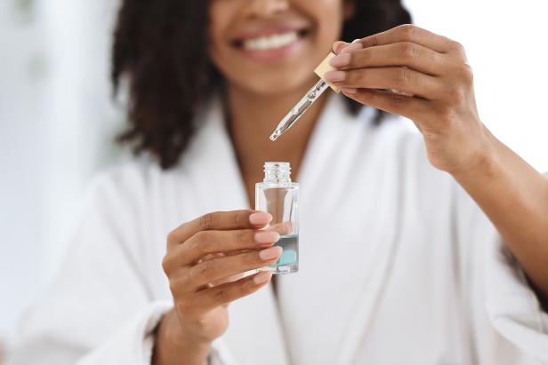 Beauty And Skincare. Smiling Black Woman Holding And Opening Bottle With Moisturizing Face Serum, Making Skin Treatment At Home, Closeup