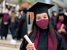 Portrait of a happy graduate student holding her diploma and wearing a facemask at her graduation during the COVID-19 pandemic