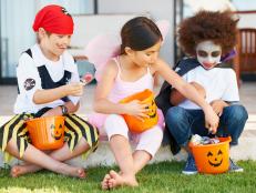 Children dressed in Halloween costumes holding candy buckets while sitting down
