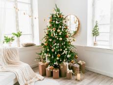 White and spacious domestic living room decorated with Christmas fir tree and pastel holiday decor. Festive craft gift boxes and wrapped presents for family and friends. Cozy celebrations at home