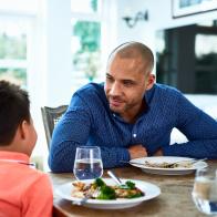 Mature man leaning forward towards boy, food on dining room table, family meal time, conversation, bonding