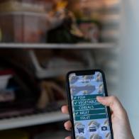 Crop anonymous person using mobile phone to buy groceries with smart application while checking fridge at home. Person buying food supplies with mobile app.