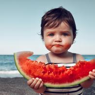 funny little girl on the beach eating watermelon and making funny face.