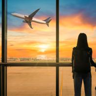 Travel tourist standing with luggage watching sunset at airport window. Woman looking at lounge looking at airplanes while waiting at boarding gate before departure. Travel lifestyle. Transport and travel concept