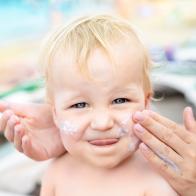 Mother applying sunscreen protection creme on cute little toddler boy face. Mom using sunblocking lotion to protect baby from sun during summer sea vacation. Children healthcare at travel time.