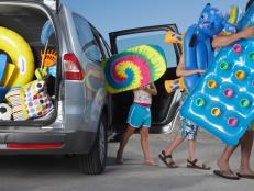 Father and two children (6-11) unloading beach accessories from car
