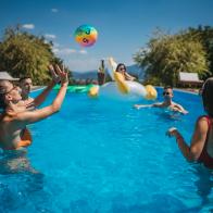 Group of young friends playing with beach ball on swimming pool