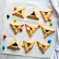 Top view hamantaschen cookies and colorful candies on a baking paper with napkin on a gray background.