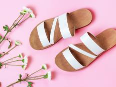 A pair of white sandals and flowers on a pink background top view.