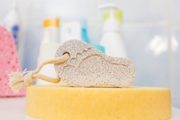 Pumice stone in foot shape on yellow bath sponge. Bathroom objects. Pedicure essentials.