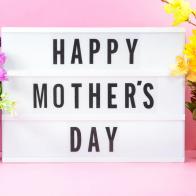 Happy Mothers Day text on light box with flowers on the background.