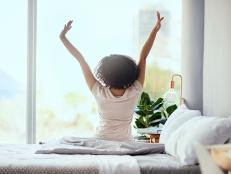 Shot of a young woman sitting on the bed in the morning and stretching