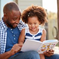 Young black father and daughter reading book outside