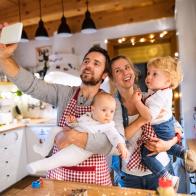 Beautiful young family making cookies at home. Father, mother. toddler boy and baby taking selfie with a smartphone.