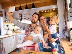 Beautiful young family making cookies at home. Father, mother. toddler boy and baby taking selfie with a smartphone.