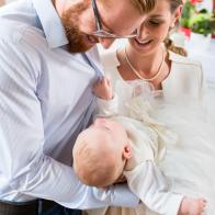 Young parents at the church with their baby wearing a christening gown