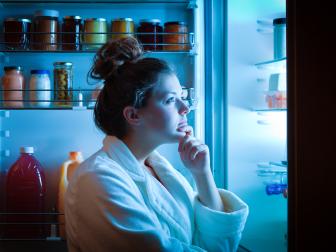 A young dieting woman standing in front of the refrigerator, contemplating and thinking about what to eat for hunger. Making choices and decision for healthy lifestyle