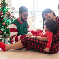 Beautiful family celebrating christmas wearing christmas pajamas and couple playing with their loving daughter at home all looking very happy