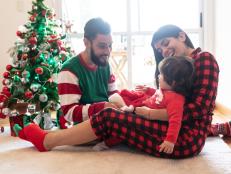 Beautiful family celebrating christmas wearing christmas pajamas and couple playing with their loving daughter at home all looking very happy