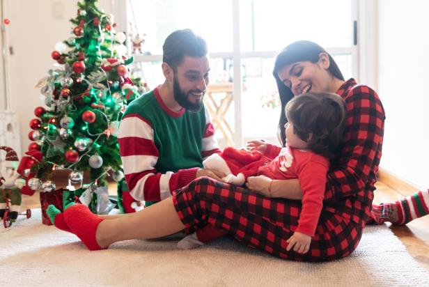 Beautiful family celebrating christmas wearing christmas pajamas and couple playing with their loving daughter at home all looking very happy