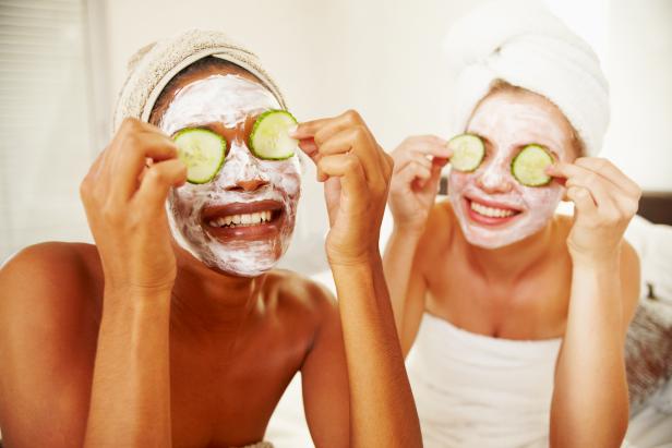 Multi-racial young women holding cucumbers over their eyes wearing face masks