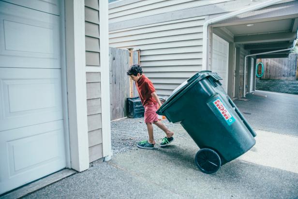 Mixed race boy pulling trash can in driveway