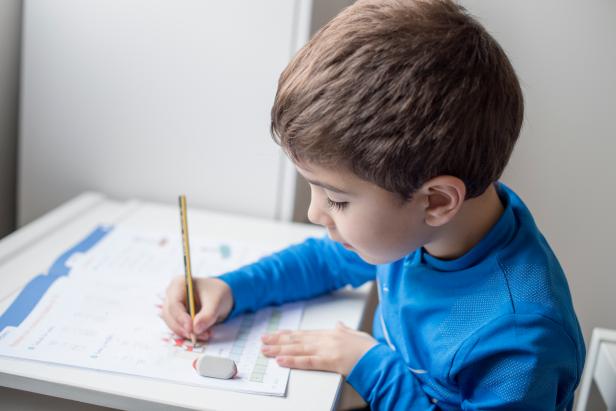 Boy sitting at table doing homework with pencil