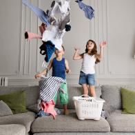 France, Provence, Marseille, living room. Siblings standing on the couch, throwing laundry in the air, smiling.