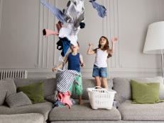 France, Provence, Marseille, living room. Siblings standing on the couch, throwing laundry in the air, smiling.