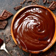 Chocolate ganache in a wooden bowl on a dark slate or rusty metal background.Top view with copy space.