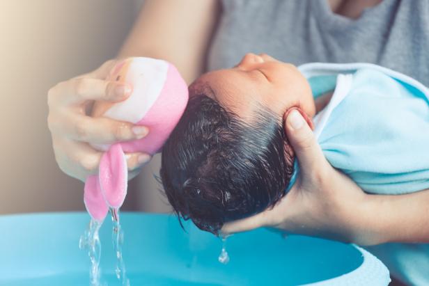 Cute asian newborn baby girl take a bath. Mom cleaning her baby hair with sponge.