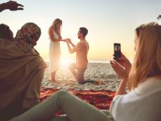 Young man proposing to woman on sunny summer beach with friends