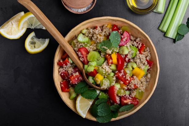 Quinoa salad with red and yellow bell peppers tomatoes, celery and grapes in the bowl on gray background ready to eat viewed from above