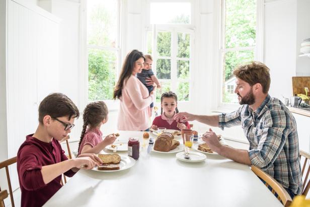 Father sitting with two girls and pre adolescent boy enjoying breakfast together in dining room