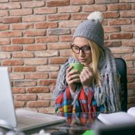 Young businesswoman suffering with flu having hot drink at work