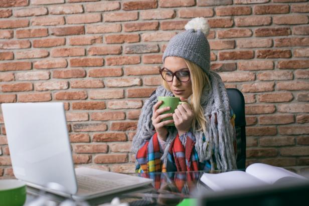 Young businesswoman suffering with flu having hot drink at work