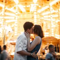 Young Caucasian heterosexual  kissing near the marry-go-round in the park