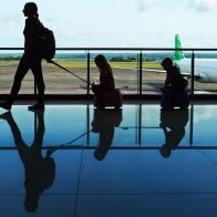 Mother with kids walk to flight boarding in airport transit hall and look through the window at airplane near departure gate. Active family lifestyle, travel by plane with children on summer vacation.