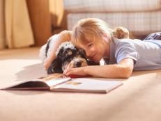 little girl cudding her dog whilst reading from her story book .