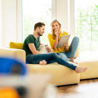 Couple sitting on couch in their new home, using digital tablet