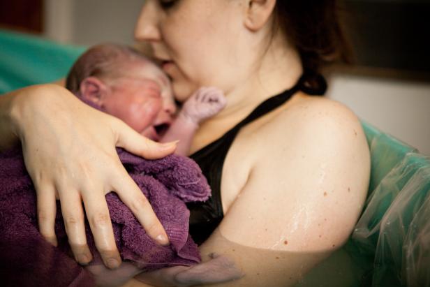 Color photo of a loving mother holding her newborn baby son in the water of a birthing tub immediately after a water birth at home.