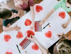 An overhead view of a family making heart shaped Valentine cards for the holiday.  Could also be a daycare or elementary school depiction.