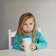 Young toddler girl holding a cup with milk in her cheeks