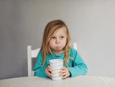 Young toddler girl holding a cup with milk in her cheeks