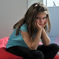 Upset young girl sitting on a bean bag at home balcony looking at the camera.